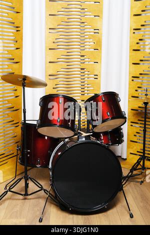Vibrant drum set in red and black colors, set against a textured yellow wall, creating a dynamic atmosphere for music creation and artistic expression Stock Photo