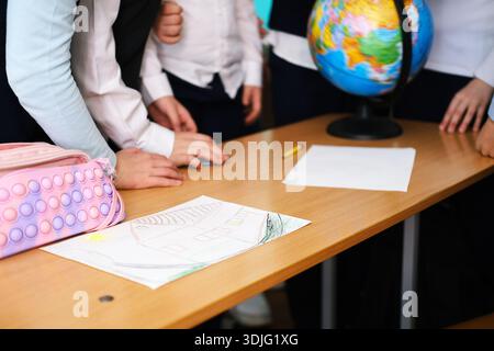 Children from various backgrounds are gathered around a table, displaying their artwork and a globe, fostering creativity and teamwork in an education Stock Photo