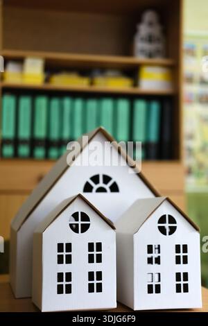 Paper houses of different sizes, featuring detailed windows and roofs, arranged on a school desk with vibrant folders, highlighting children's craftin Stock Photo