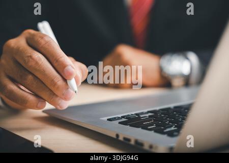 A man hand closeup in a pose to sign an electronic document, a formal gesture with a digital pen above a laptop, a sign of a new business contract or Stock Photo