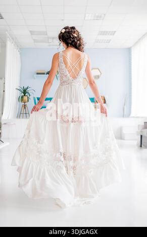 Woman in a stunning white gown with lace accents poses elegantly in a bright, contemporary space, highlighting fashion and grace in a tranquil setting Stock Photo