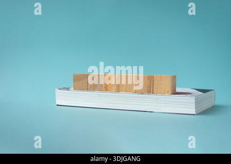 6 square wooden blocks in a row on top of a closed book. Light blue background. Stock Photo