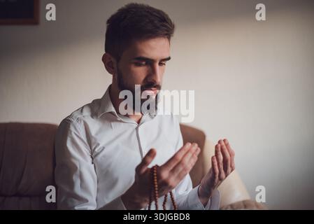 A Muslim prayer man praying with hands up at home. Stock Photo