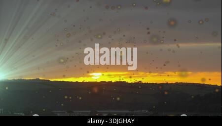 Showing orange sunset band over rolling hills in rural view, droplets on glass and green flare Stock Photo