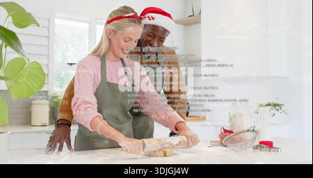Rolling woman in pink sweater and green apron, man guiding dough in kitchen with rolling pin Stock Photo