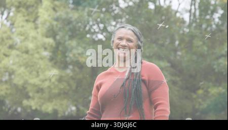 Smiling senior woman wearing rust sweater and showing long dreads in park, with small white crosses Stock Photo