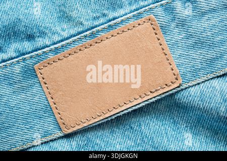 Empty patch label stitched on light blue denim fabric background closeup Stock Photo