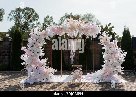 A beautifully arranged wedding arch adorned with lush white and pink flowers, cascading greenery, and hanging beaded drapes, set against a serene gard Stock Photo