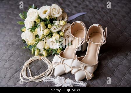 A beautifully styled bridal arrangement featuring white pointed-toe heels with pearl embellishments, a delicate bouquet of white roses and greenery, a Stock Photo