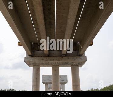 Underside of a concrete bridge under construction with parallel beams and cylindrical piers forming strong symmetry over a river landscape. Stock Photo