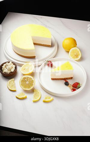 A beautifully presented whole lemon mousse cake, with a slice cut out, sits alongside a single serving on a plate. Garnished with vibrant strawberries Stock Photo
