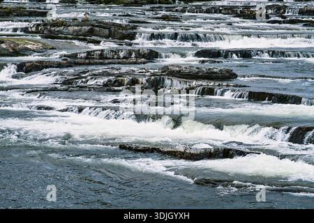 Trappstegsforsen waterfall creating multiple small cascades and frothy white water as the river flows over dark rock formations, showcasing the serene Stock Photo