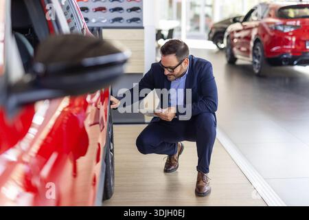 Professional salesman checking out wheels and tires of a new car at the dealership car dealer helping his customer man buying choosing automobile luxu Stock Photo