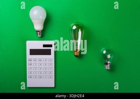 White calculator and incandescent lamps or LED bulb on green background. Concept showing the payment of electricity bills. The concept of savings elec Stock Photo