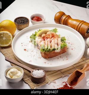 Delicious shrimp cocktail on toasted bread, garnished with lemon and paprika, served with assorted condiments and seasonings on a white plate, on a ma Stock Photo