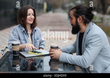 Caucasian couple talking at outdoor cafe with coffee and laptop Stock Photo