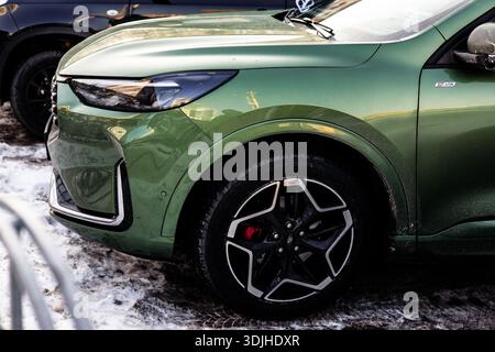 KYIV, Ukraine 20 January 2026 Modern green crossover car parked on snow, close-up of front wheel and LED headlight. Stock Photo