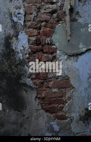 Exposed brickwork reveals layered plaster decay, highlighting aging construction materials and surface deterioration. Stock Photo
