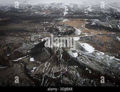 Aerial view of stark volcanic cones punctuate the snowy, windswept landscape, their dark forms contrasting against the white and brown earth, Flugir, Stock Photo