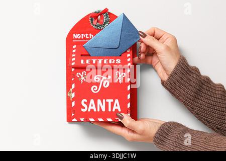 Hands placing envelope into decorative letter to Santa mailbox. Christmas tradition concept showing holiday preparation childhood memories. Stock Photo