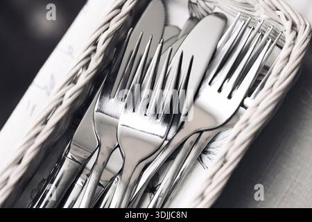 Clean cutlery set in basket closeup. Forks and knives organized after washing. Kitchen hygiene routine. Stainless steel utensils detail. Stock Photo