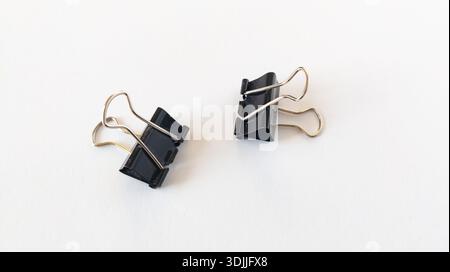 Small binder clips, black paper clips for office supplies, bulldog clips, metallic stationery clips arrange isolated on white background. Stock Photo