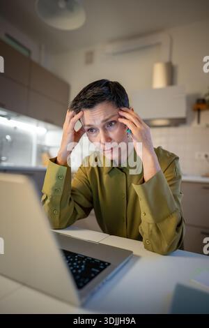 Senior businesswoman with migraine staring at laptop screen, dealing with heavy stress at work. Stock Photo