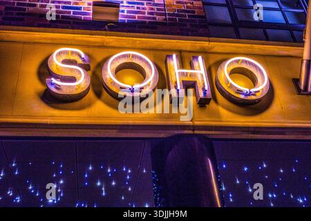 Warm neon glowing signage for SOHO Coffee Co. mounted on a brick and stone facade at night in the Canary Wharf district, London, UK. Stock Photo