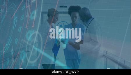 Reviewing clinical data three staff in scrubs, lab coats using tablet, HUD in hospital corridor Stock Photo