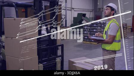 Checking laptop man wearing hardhat, safety vest in warehouse with forklift, boxes, copy space Stock Photo