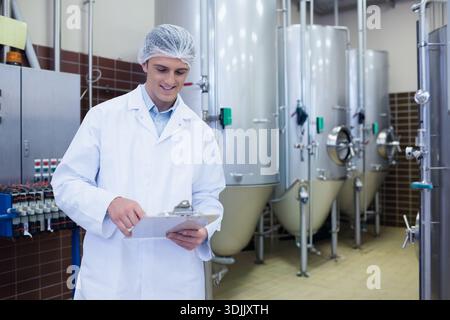 Clipboard resting on steel tanks, piping and valves running along tiled floor in food plant. Processing, facility, fermentation, vessels, pipes, conne Stock Photo