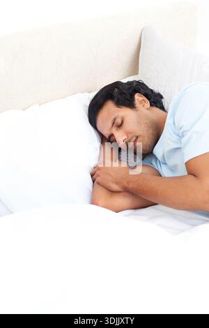 Middle-aged man lying on bed, resting on white pillow, wearing light blue shirt with duvet. Sleep, male, bedroom, minimal, monochrome, serenity, calm Stock Photo