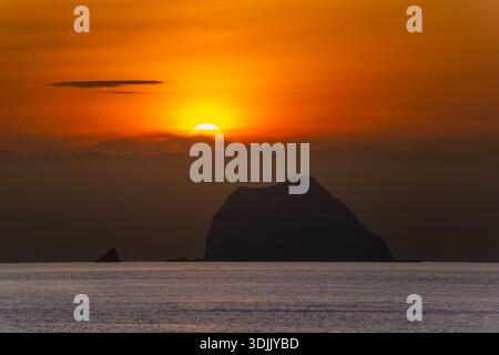 A breathtaking summer sunrise at Keelung Waimushan, Taiwan. The sun slowly emerges from behind dark clouds, illuminating the sky with a beautiful oran Stock Photo