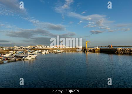 Wide panoramic view of the marina and harbor in Olhão, Algarve, Portugal. Small boats are moored on calm blue water near the harbor entrance, with por Stock Photo