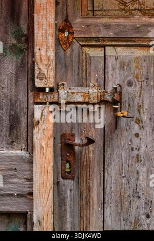 Close-up of a weathered wooden door featuring a rusty metal latch, a small yellow padlock, a vintage handle, and aged textures. Stock Photo