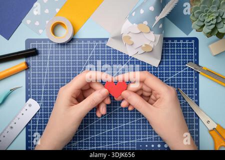Making a gnome in love craft. Hands are holding a red heart cut out of paper. Creative process. Stock Photo