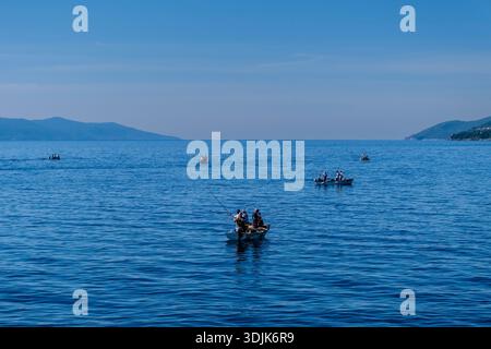 Small fishing boats on the blue sea near Ika. Anglers fishing from boats with the coastline and hills in the distance under a clear sky. Stock Photo