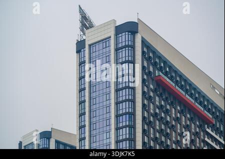 Contemporary high-rise building facade defining the urban skyline with many windows and an innovative design, featuring a prominent red accent balcony Stock Photo