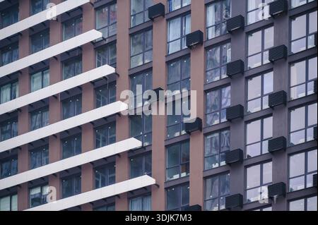 Modern apartment building showcasing a geometric facade with brown and dark grey sections, numerous windows, and structured balconies creating a patte Stock Photo