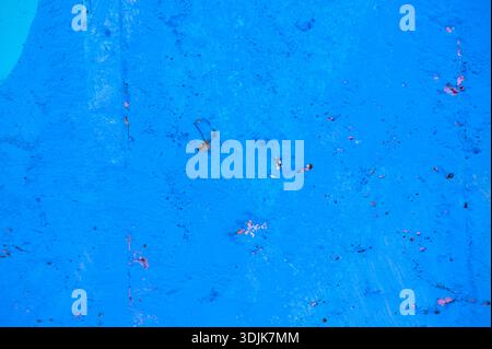 Blue painted concrete wall displaying uneven textures and rough, peeling surfaces, providing a vibrant, abstract background for various design project Stock Photo