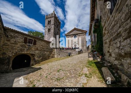 Cobblestone path leads to die Kirche St. Jerome in Hum. Group of people stands before the stone facade under a blue sky with clouds. Stock Photo