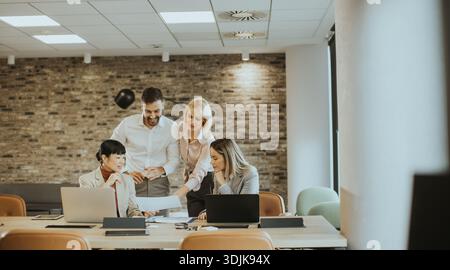 A diverse group of four professionals collaborates around a table in a bright office. They discuss documents, sharing ideas and strategies to enhance Stock Photo