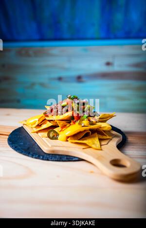 Nachos serving on a wooden board with melted cheese, beef, guacamole, and salsa Stock Photo