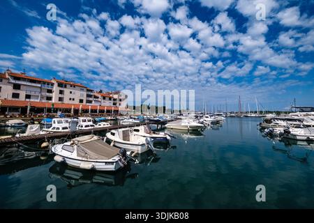 Small motorboats and white yachts are moored along piers in the marina of Cervar Porat under a blue sky with white clouds. Stock Photo