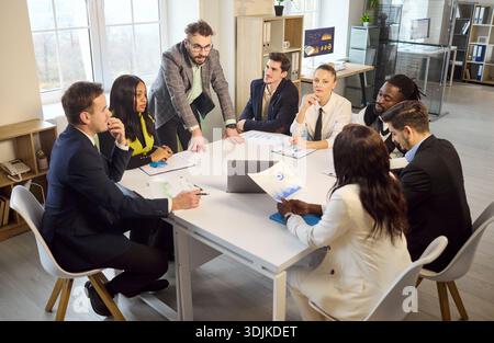 Manager leads office team briefing at table, analyzing charts and strategy Stock Photo