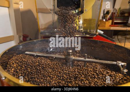 Coffee is roasted by hand in a small drum roasting machine with a lot of experience, where the finished hot coffee beans are just being poured out to Stock Photo