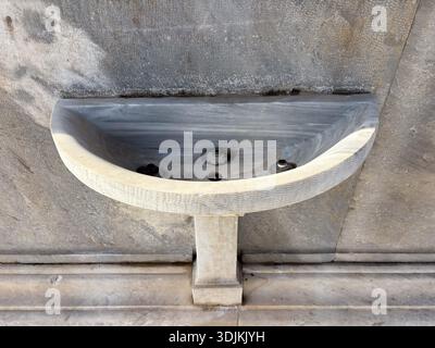 Stone washbasin / lavabo detail. Antique sink fixture with visible plumbing holes, carved marble basin, weathered texture on ancient wall. Stock Photo