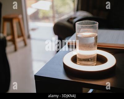 Photograph of a glass glass with water on a black table, illuminated by warm light, with an out-of-focus interior background. Ideal for hydration, hea Stock Photo