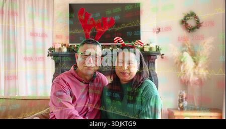 Sitting senior couple leaning on beige couch at home wearing headbands, stock tickers showing Stock Photo