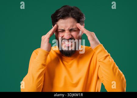 30s aged man having headache, touching temples, Suffering on green background. Stock Photo